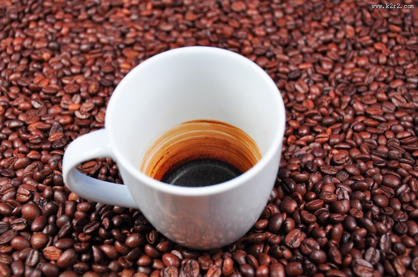 咖啡豆散落在装有咖啡的杯子旁图片大全